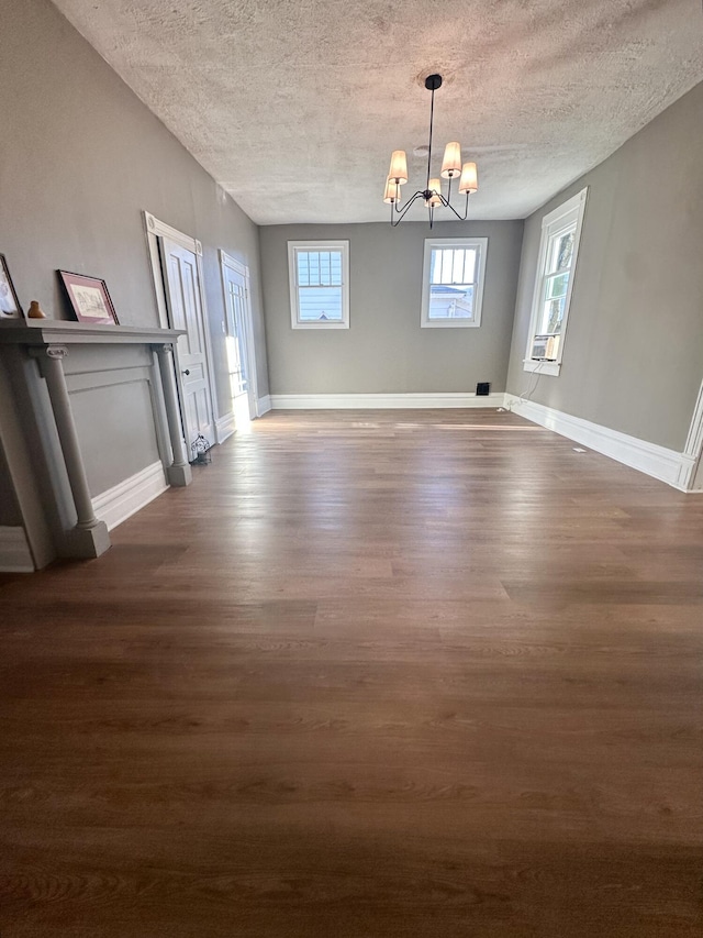 unfurnished dining area with dark wood-style floors, a textured ceiling, a chandelier, and baseboards