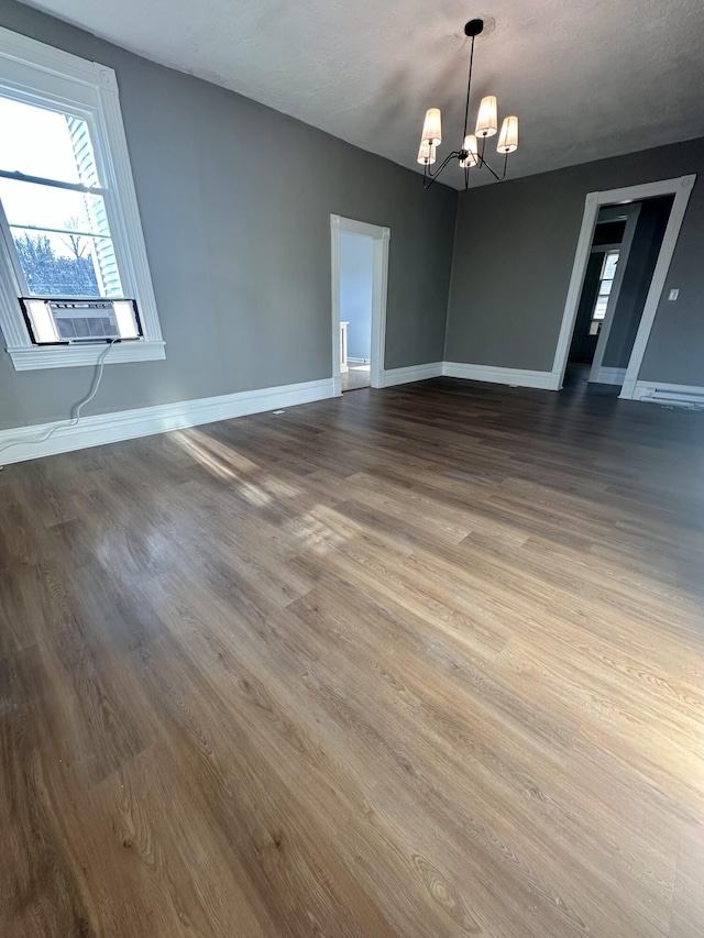 spare room with cooling unit, a notable chandelier, baseboards, and wood finished floors