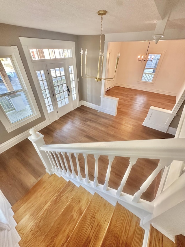 stairs featuring an inviting chandelier, a textured ceiling, baseboards, and wood finished floors