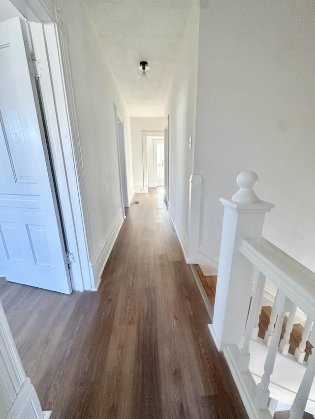 hall featuring dark wood-style floors, baseboards, and an upstairs landing