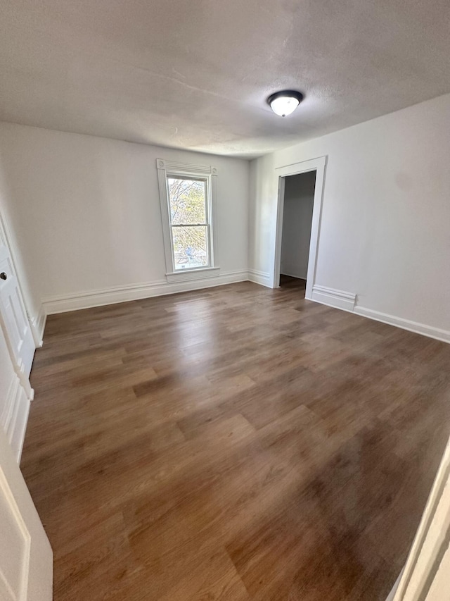 empty room with dark wood-style floors, a textured ceiling, and baseboards