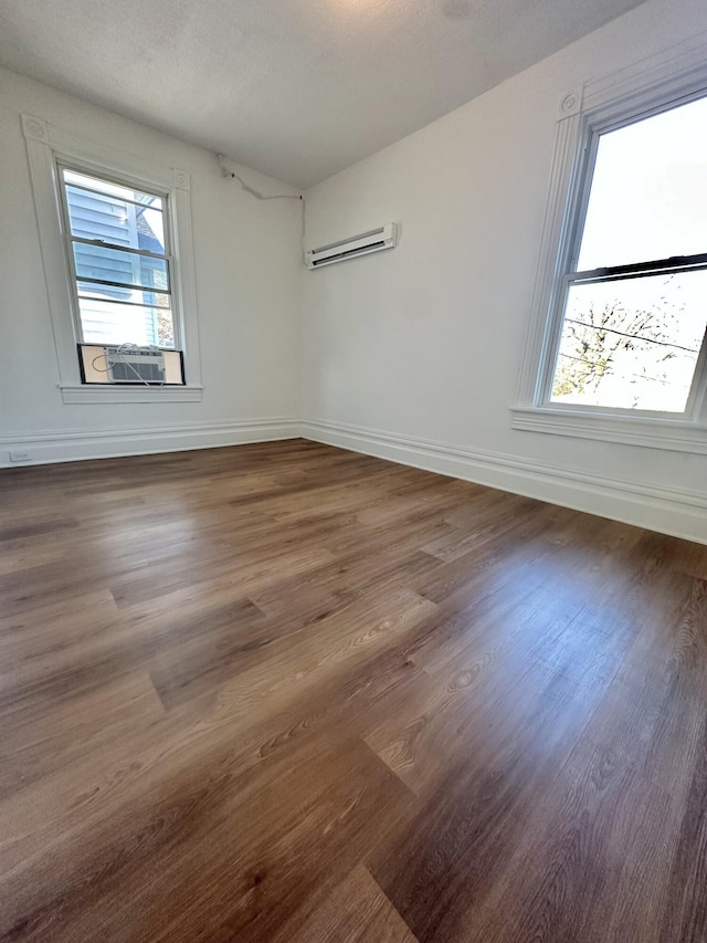 empty room featuring dark wood-style floors, a wall unit AC, lofted ceiling, and baseboards