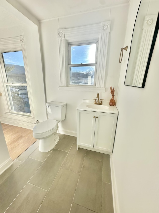 half bathroom with baseboards, vanity, and toilet