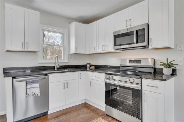 kitchen featuring appliances with stainless steel finishes, dark hardwood / wood-style floors, sink, white cabinets, and dark stone counters