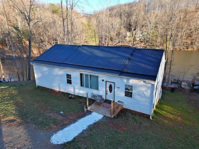 view of front of property featuring metal roof, a wooded view, and a front lawn