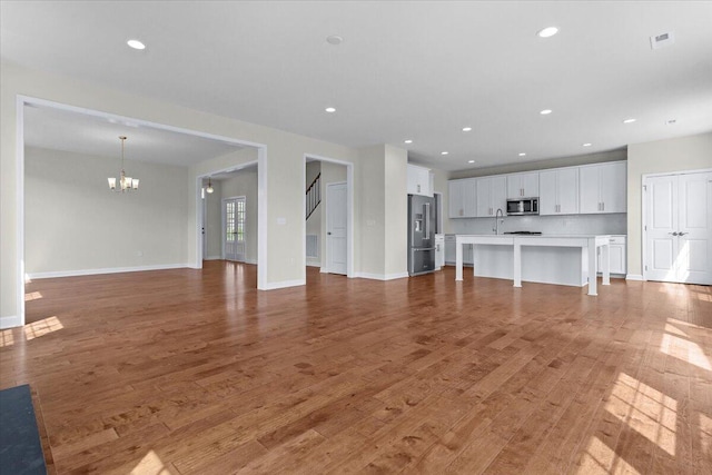 unfurnished living room featuring an inviting chandelier, sink, and hardwood / wood-style flooring