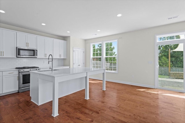 kitchen featuring stainless steel appliances, a kitchen island with sink, decorative backsplash, and white cabinets