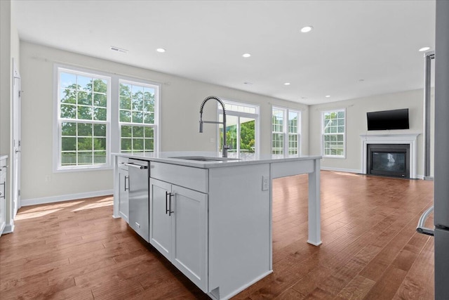 kitchen with dishwasher, wood-type flooring, sink, white cabinets, and a center island with sink