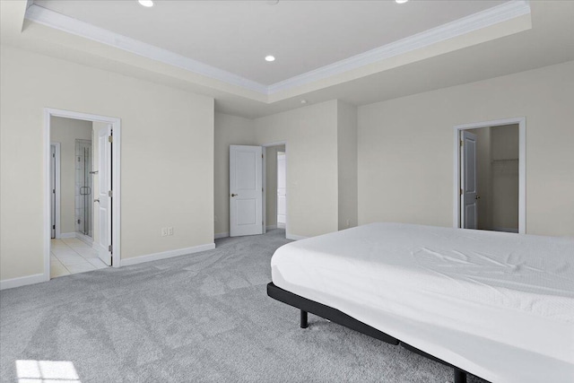 bedroom with ensuite bath, a walk in closet, light carpet, ornamental molding, and a raised ceiling