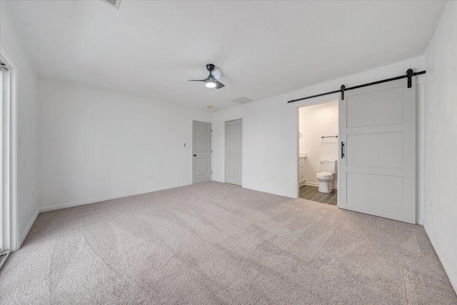 unfurnished bedroom with a barn door, light carpet, connected bathroom, and ceiling fan