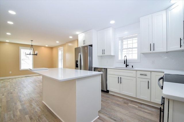 kitchen featuring decorative light fixtures, stainless steel appliances, light countertops, white cabinetry, and a sink