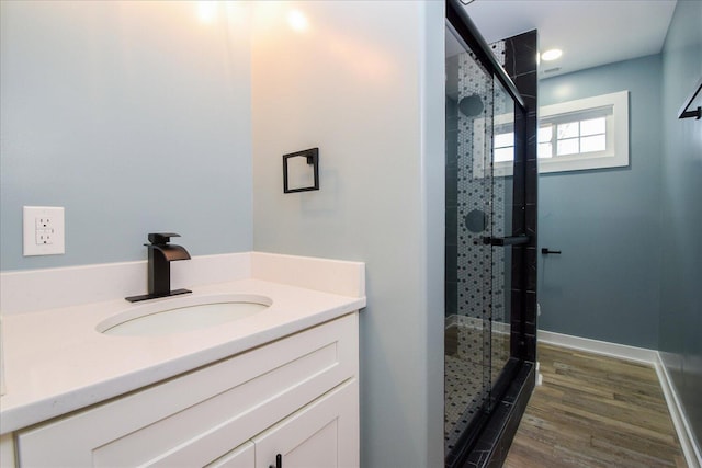 full bathroom with a stall shower, vanity, baseboards, and wood finished floors