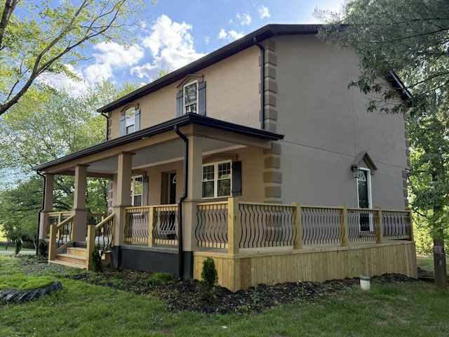 back of house with covered porch, stucco siding, and a yard