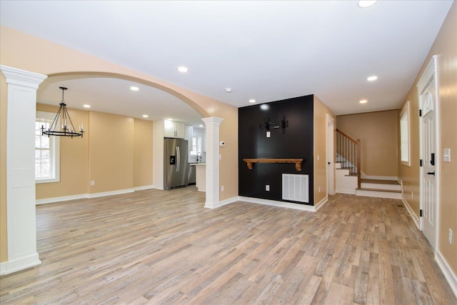 unfurnished living room with arched walkways, light wood-type flooring, visible vents, and ornate columns