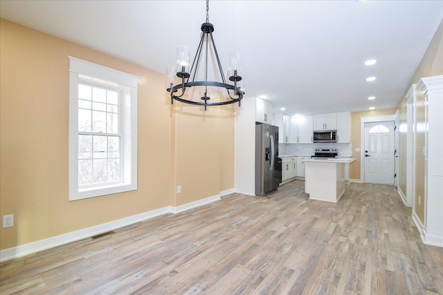 kitchen featuring stainless steel appliances, a kitchen island, white cabinets, hanging light fixtures, and light countertops