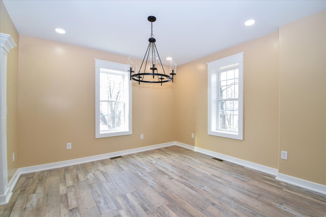 empty room with a wealth of natural light, a chandelier, visible vents, and wood finished floors