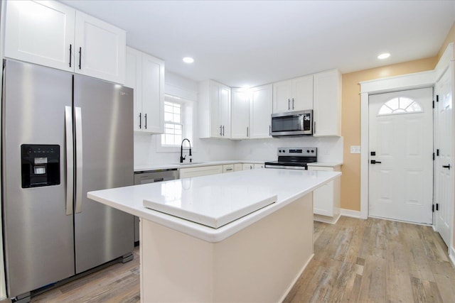 kitchen featuring stainless steel appliances, white cabinets, light countertops, light wood-type flooring, and a center island