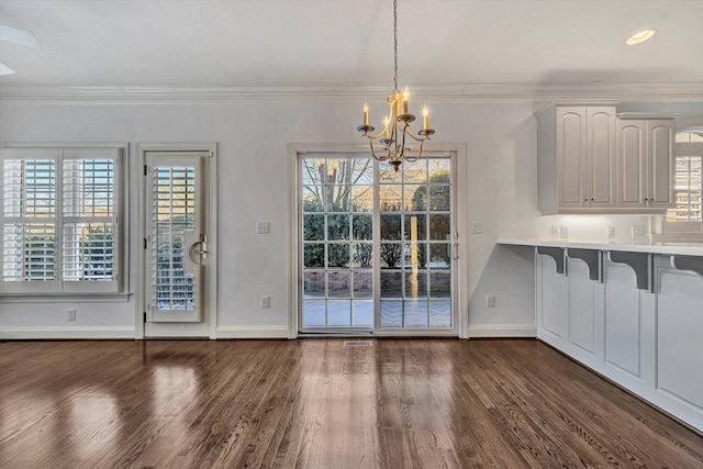 unfurnished dining area with dark wood-type flooring, ornamental molding, and a chandelier