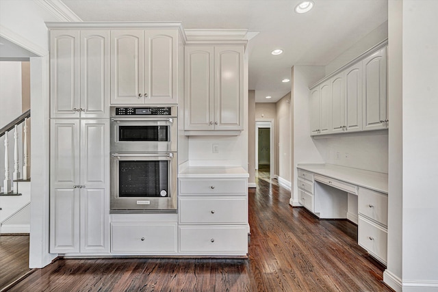 kitchen featuring stainless steel double oven, dark hardwood / wood-style flooring, built in desk, and white cabinets