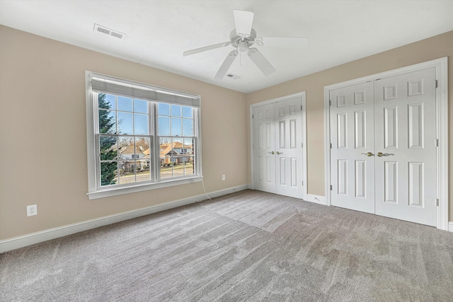 unfurnished bedroom with light carpet, two closets, and ceiling fan