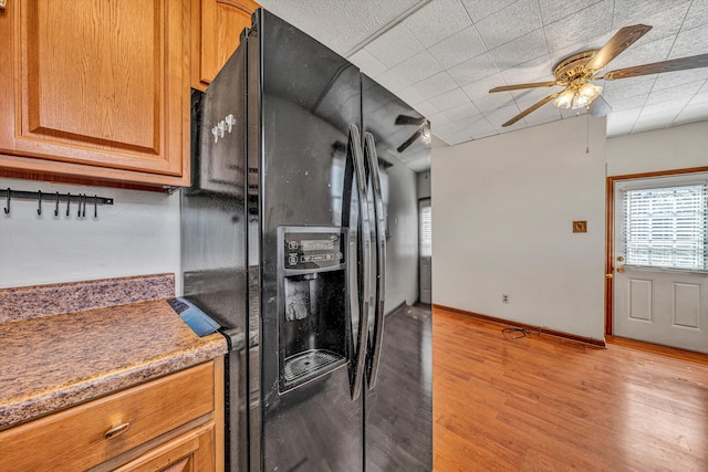 kitchen with baseboards, brown cabinetry, light wood-style floors, ceiling fan, and black fridge with ice dispenser