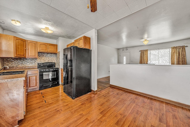 kitchen with light countertops, light wood-style flooring, a sink, black appliances, and backsplash