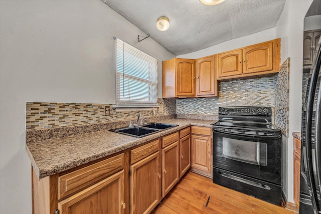 kitchen with light wood finished floors, a sink, a textured ceiling, backsplash, and black appliances