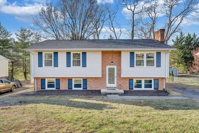 bi-level home featuring a front lawn, brick siding, a chimney, and fence