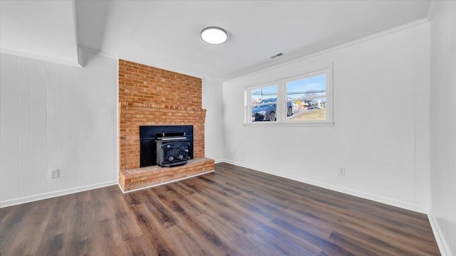 unfurnished living room featuring dark wood-style floors, a wood stove, ornamental molding, and visible vents