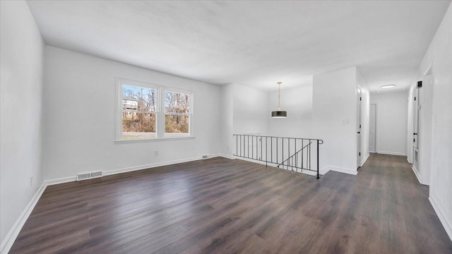 spare room with dark wood-style flooring, visible vents, and baseboards