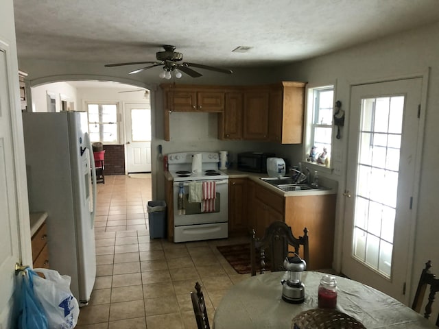 kitchen with white appliances, arched walkways, light countertops, a sink, and light tile patterned flooring