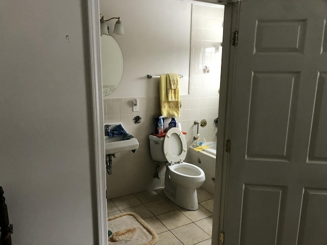 bathroom with tile walls, toilet, wainscoting, a sink, and tile patterned floors