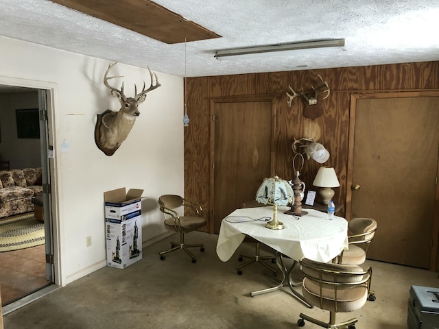 dining room with concrete floors, wooden walls, and a textured ceiling