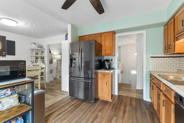 kitchen with tasteful backsplash, brown cabinetry, dark wood-type flooring, black appliances, and a sink