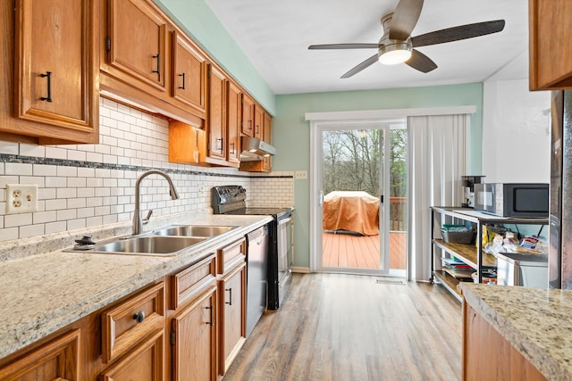 kitchen with light stone counters, under cabinet range hood, a sink, brown cabinets, and black appliances