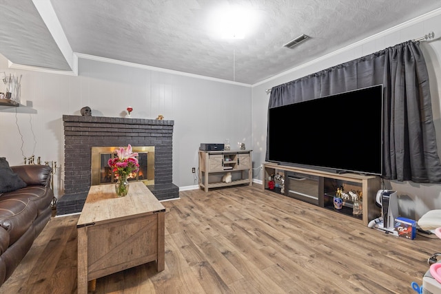 living area featuring a textured ceiling, a fireplace, wood finished floors, visible vents, and crown molding