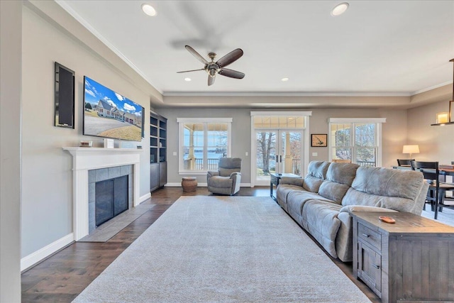 living room featuring baseboards, dark wood-type flooring, crown molding, a fireplace, and recessed lighting