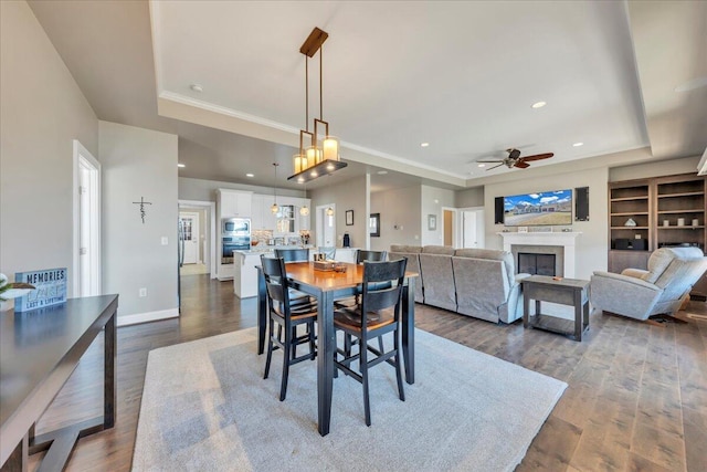 dining room with a tray ceiling, dark wood-style flooring, a fireplace, and baseboards