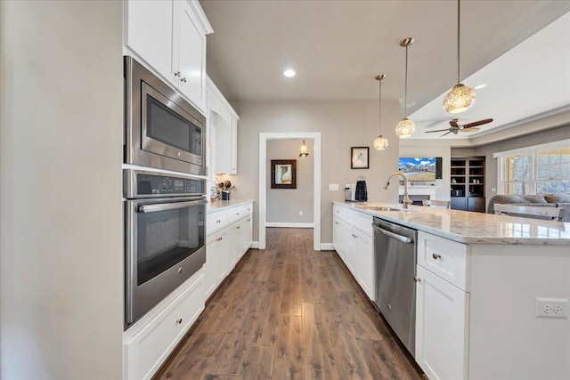 kitchen featuring stainless steel appliances, a peninsula, a sink, open floor plan, and dark wood-style floors