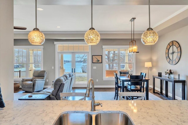 kitchen featuring baseboards, light stone counters, crown molding, french doors, and a sink