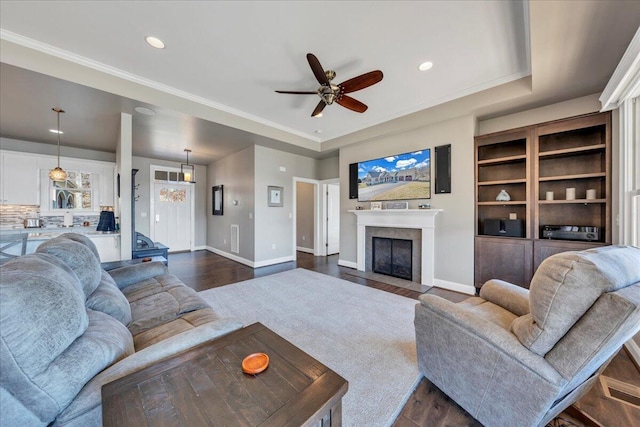 living room featuring dark wood-style flooring, a tiled fireplace, a raised ceiling, and baseboards