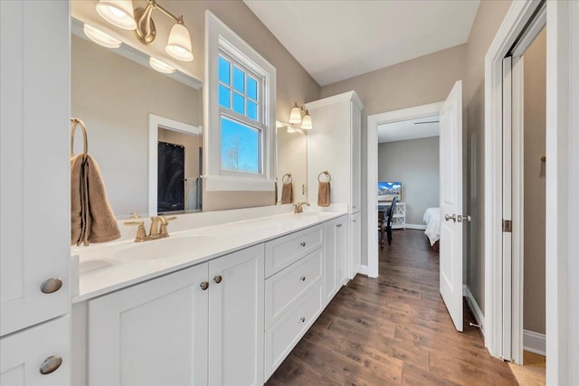 ensuite bathroom featuring double vanity, wood finished floors, a sink, and baseboards