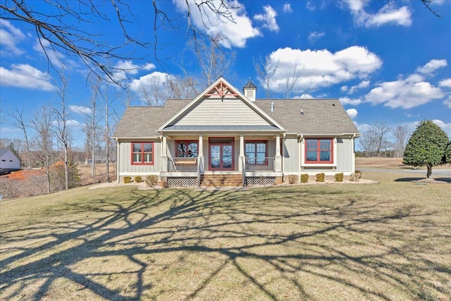 view of front of house with covered porch, roof with shingles, a chimney, and a front lawn