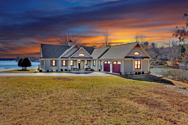 view of front of home with a garage, concrete driveway, a water view, and a front lawn