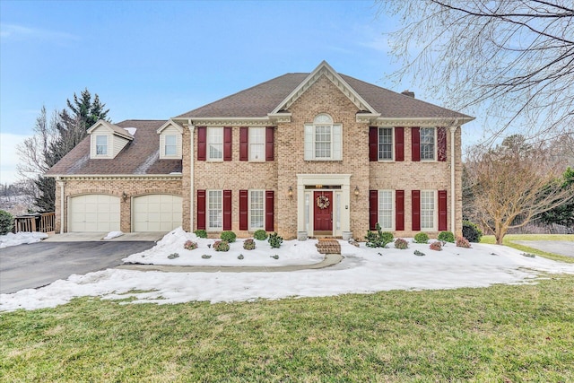 view of front of house featuring aphalt driveway, brick siding, roof with shingles, a front yard, and a garage