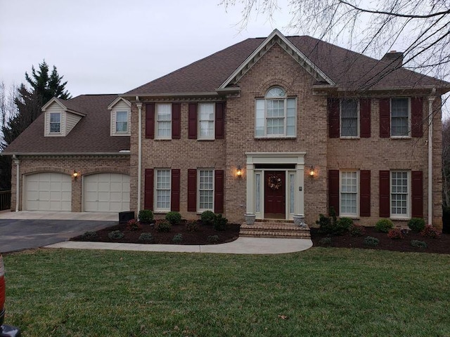view of front facade featuring roof with shingles, an attached garage, driveway, a front lawn, and brick siding