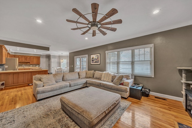 living area featuring light wood finished floors, ceiling fan with notable chandelier, crown molding, and baseboards