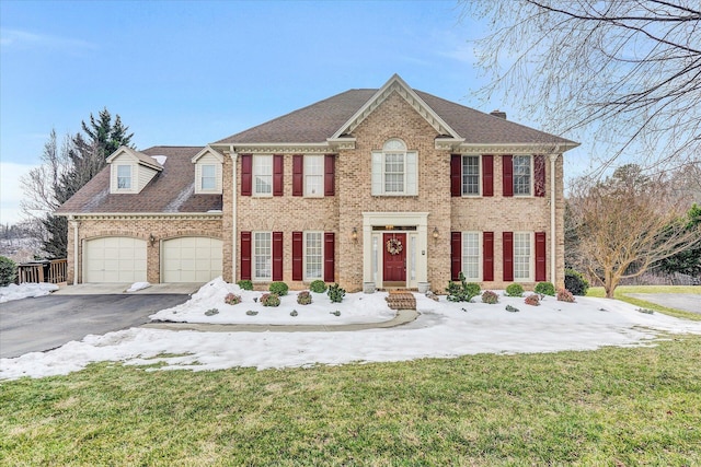 view of front facade with roof with shingles, brick siding, aphalt driveway, a front lawn, and a garage