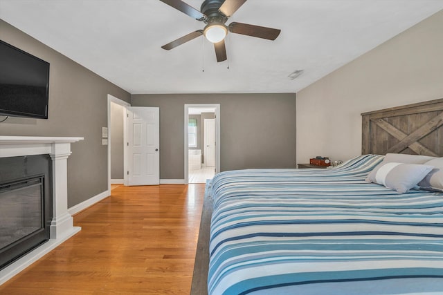 bedroom featuring visible vents, light wood-style flooring, baseboards, ceiling fan, and a glass covered fireplace