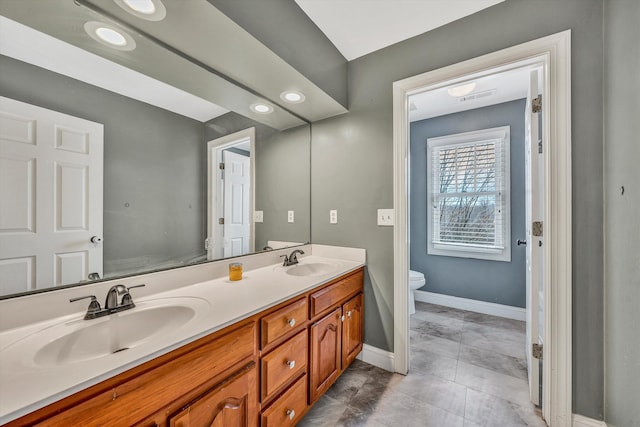 full bathroom featuring baseboards, double vanity, a sink, and toilet